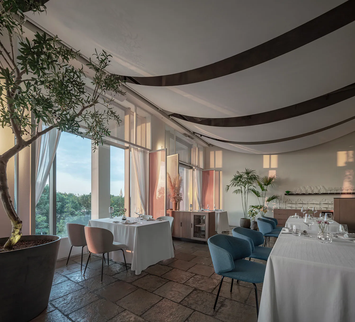A modern restaurant interior with large windows, elegant seating, and greenery.