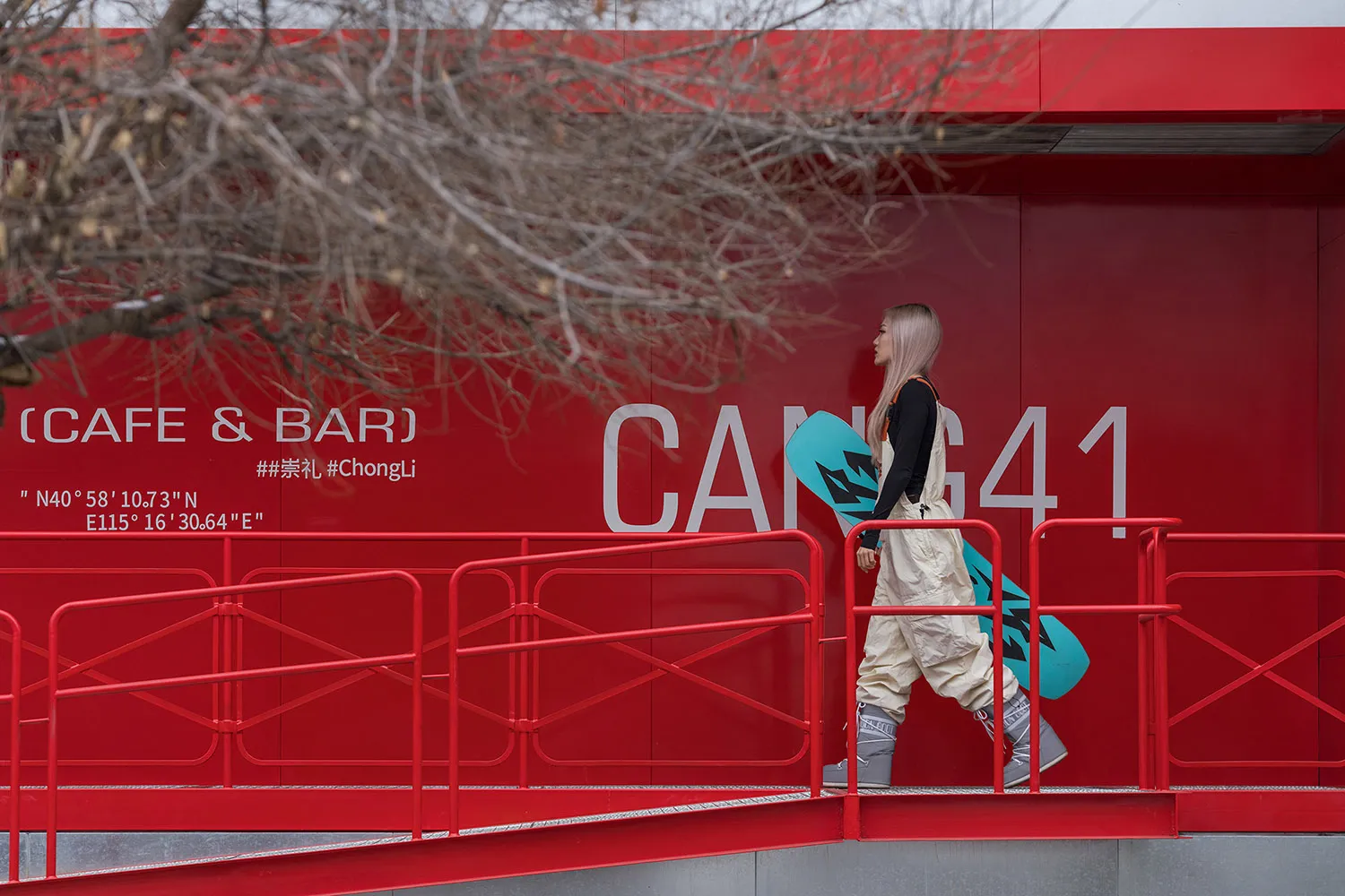 A woman walking on a red metal bridge over a red wall with the text 'CAFE & BAR CAMG41' and '#ChongLi'.