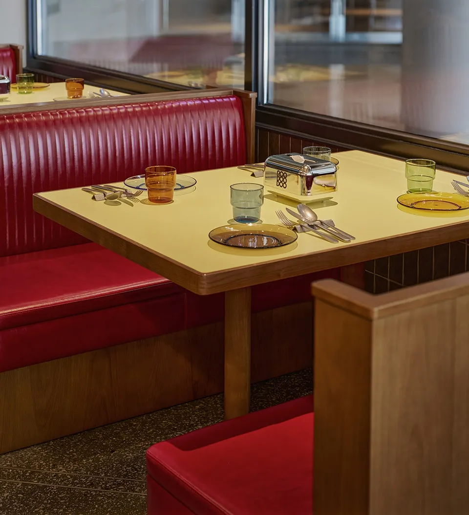 A restaurant interior with a red leather dining table set with plates, glasses, and cutlery.