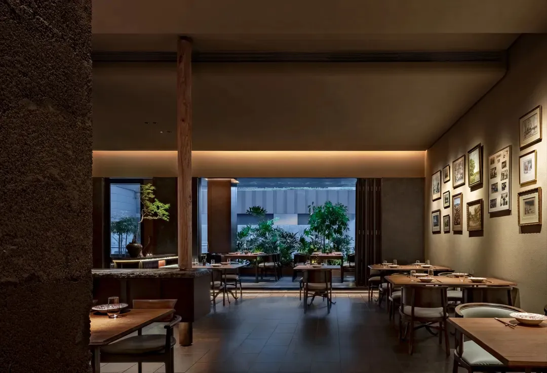 A modern restaurant interior featuring wooden tables, stone details, and green plants.