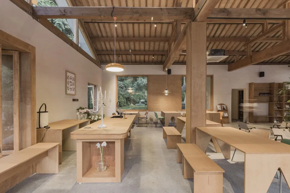 A modern cafe interior with wooden furniture and a long central table.