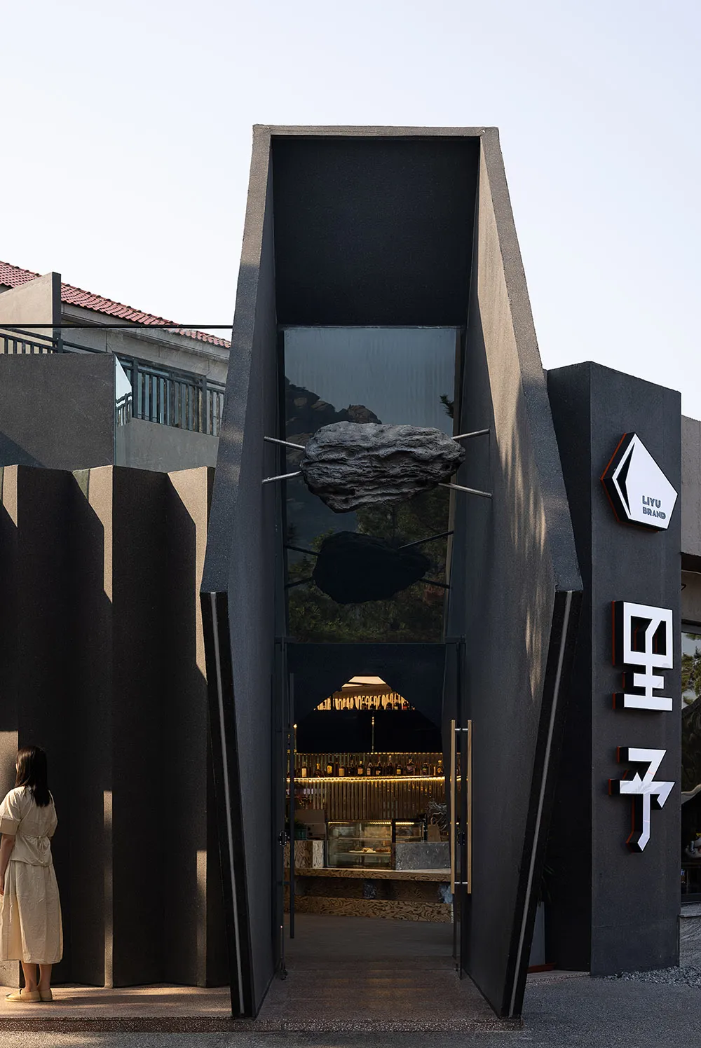 A modern storefront with black metal and glass elements, featuring a metallic cloud sculpture.