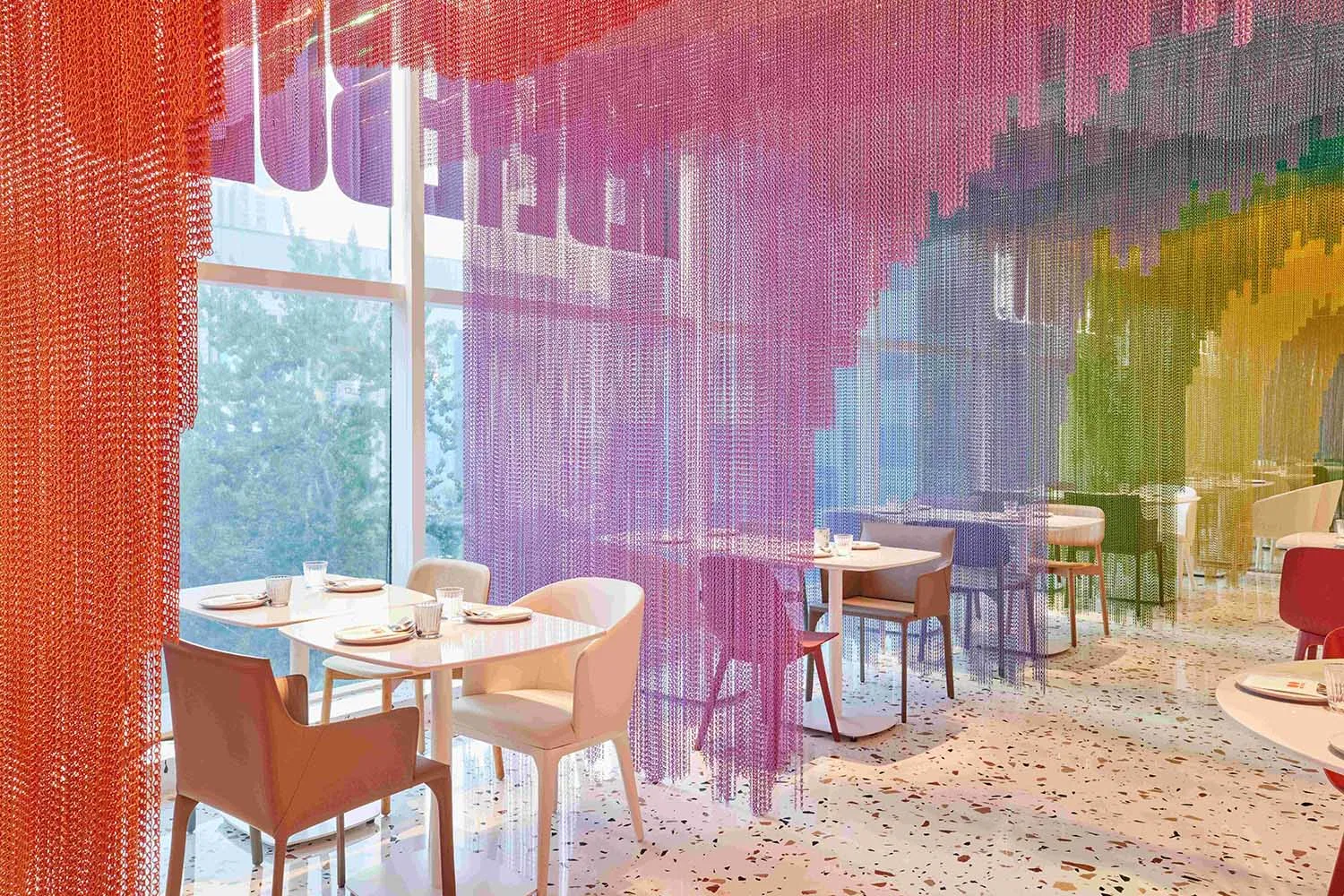 A café interior with colorful chain link drapery hanging from the ceiling, creating a vibrant and modern atmosphere.