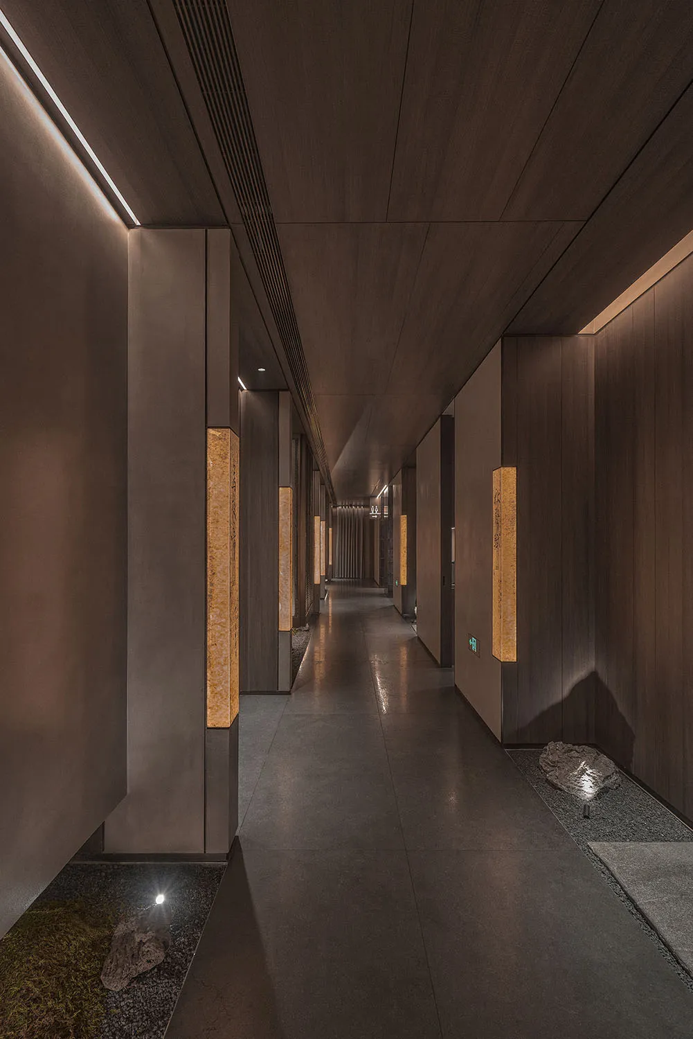A minimalist hotel corridor with wooden walls and concrete flooring.