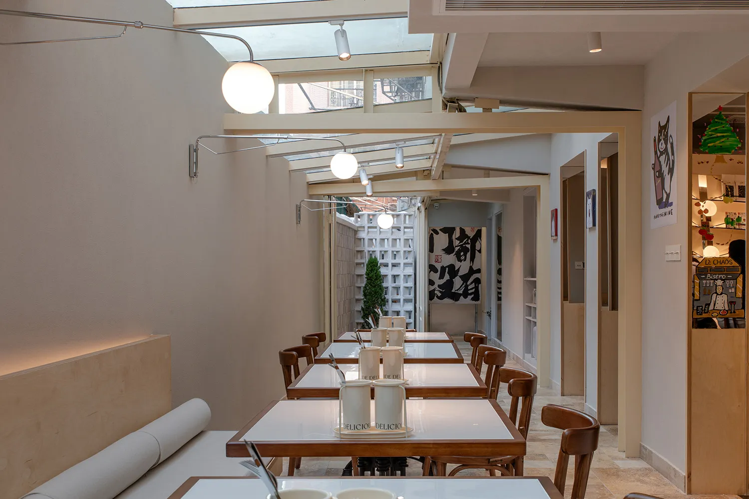 A minimalist restaurant with white walls, wooden tables, and modern lighting fixtures.