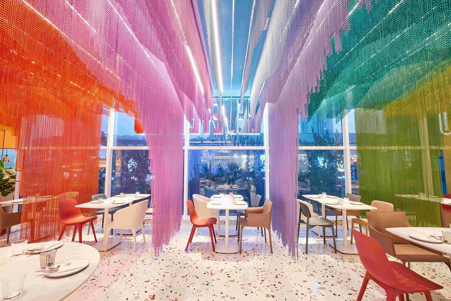 A modern restaurant with colorful terrazzo flooring and hanging rainbow curtains.