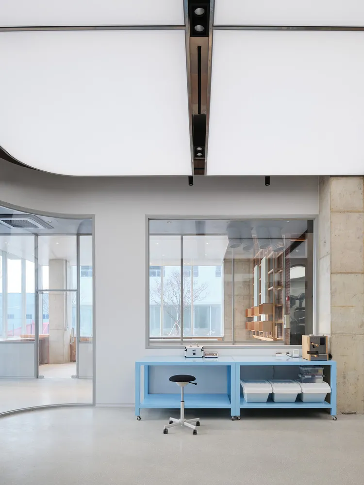 A modern, minimalist workstation with a blue table and a black stool in an open office space.
