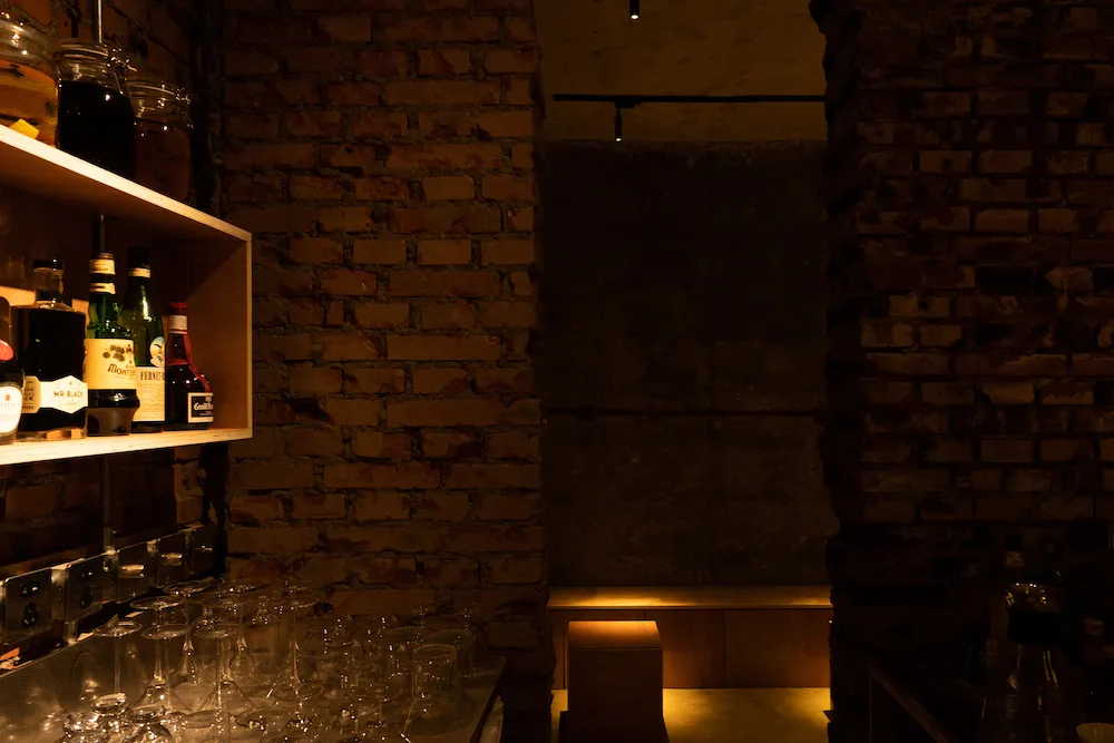 An industrial-style wine bar featuring exposed brick walls and a variety of wine bottles and glasses on shelves and tables.