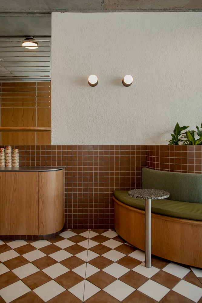 A modern cafe interior with a wooden floor, tiled walls, and green cushioned seating.