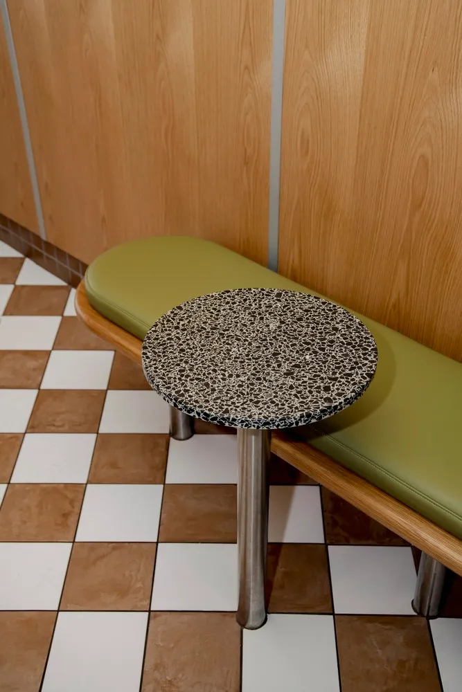 A modern restaurant interior with a round, speckled black countertop on a checkered tile floor.
