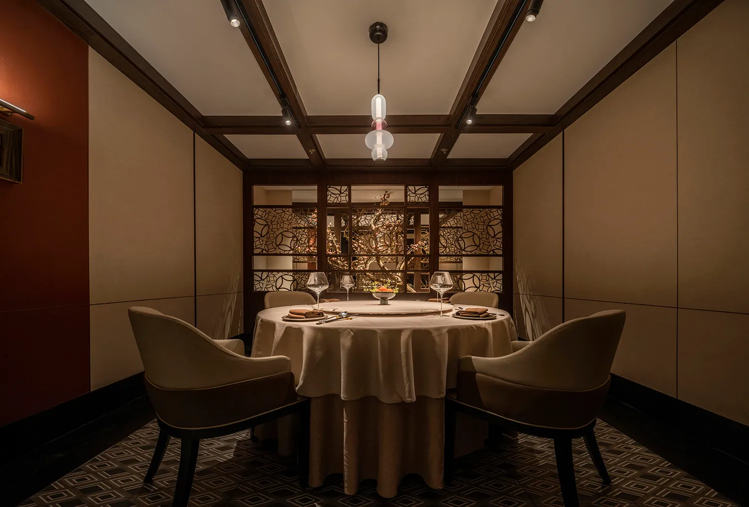 A modern restaurant interior with a round table set for a meal, featuring wood chairs and a circular light fixture.