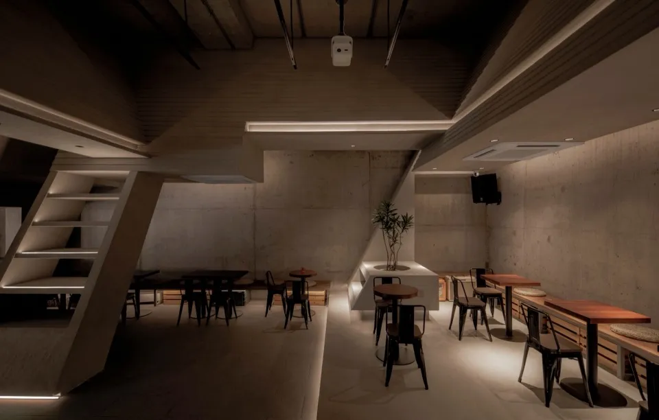 A modern, industrial-themed restaurant with concrete walls, wooden tables, and metal chairs.