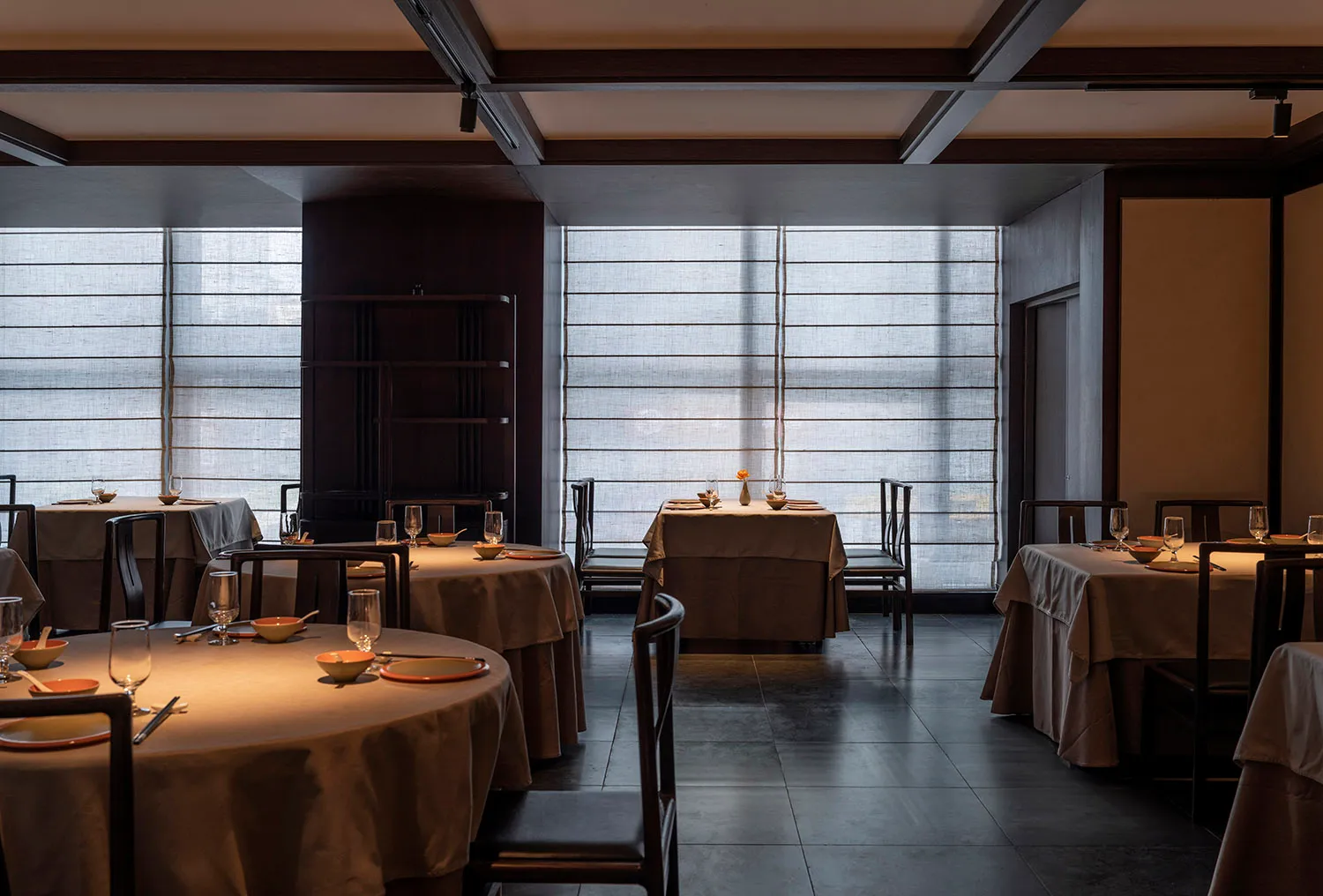 A modern restaurant interior with round tables, chairs, and upholstered seating arranged in a spacious, open layout.