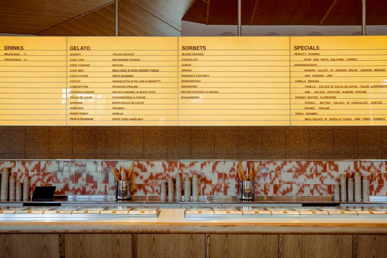 Gelato counter with tiled countertop displaying menu offerings.