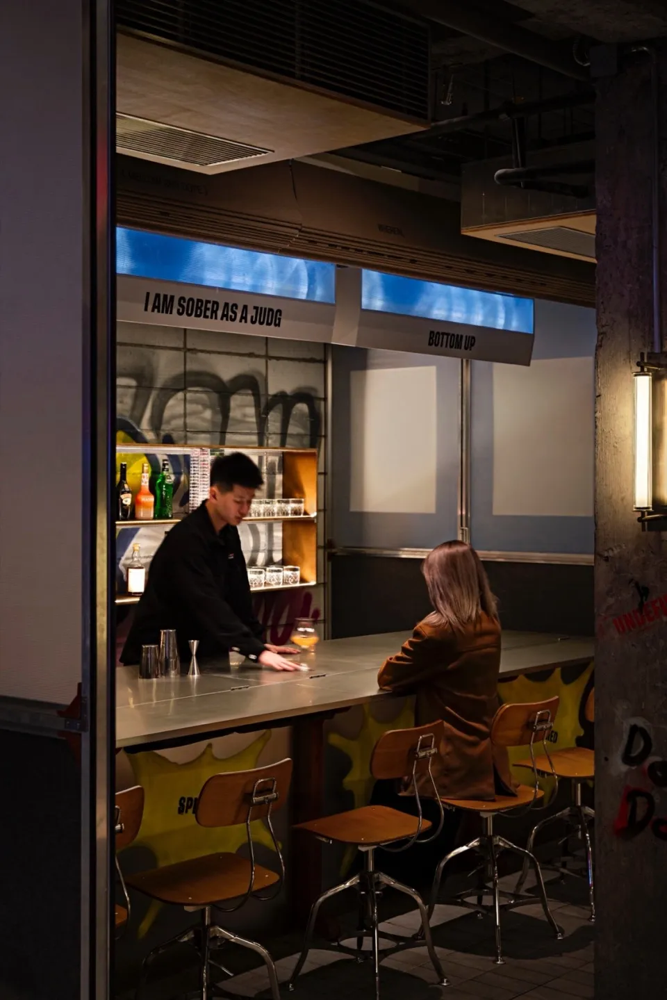 Bar interior with metallic bar top and stools, industrial design aesthetic.