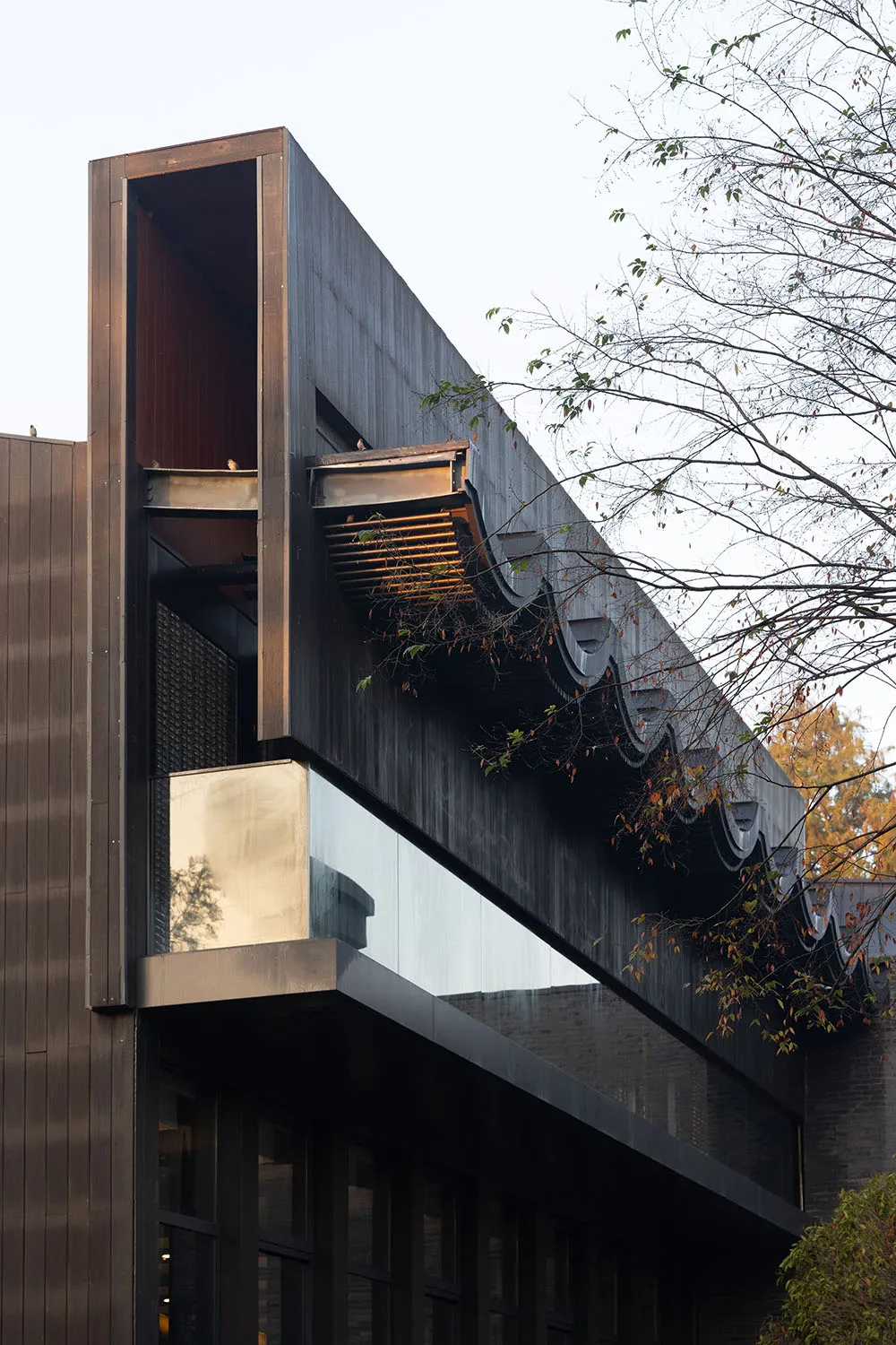 A modern building exterior clad with dark metal material, featuring geometric shapes and large glass windows.