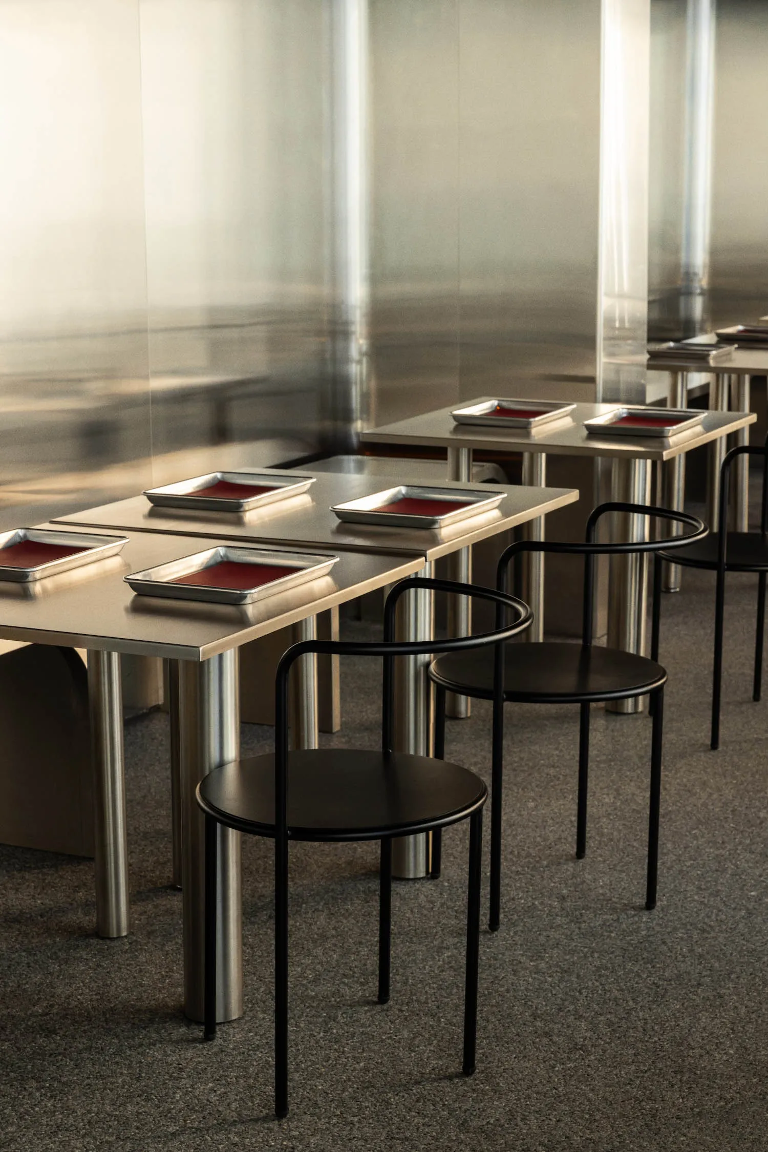 A sleek, modern restaurant interior featuring metal and black tables and chairs with red dishes.