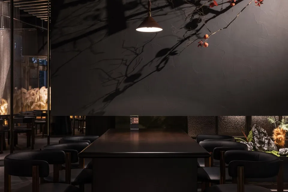 A modern restaurant interior with black walls, dark wood furniture, and a black stone counter, featuring a patterned glass pa