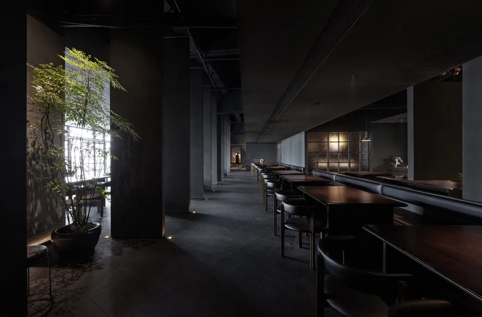 Modern restaurant interior with concrete walls, glass panels, and metal furniture.