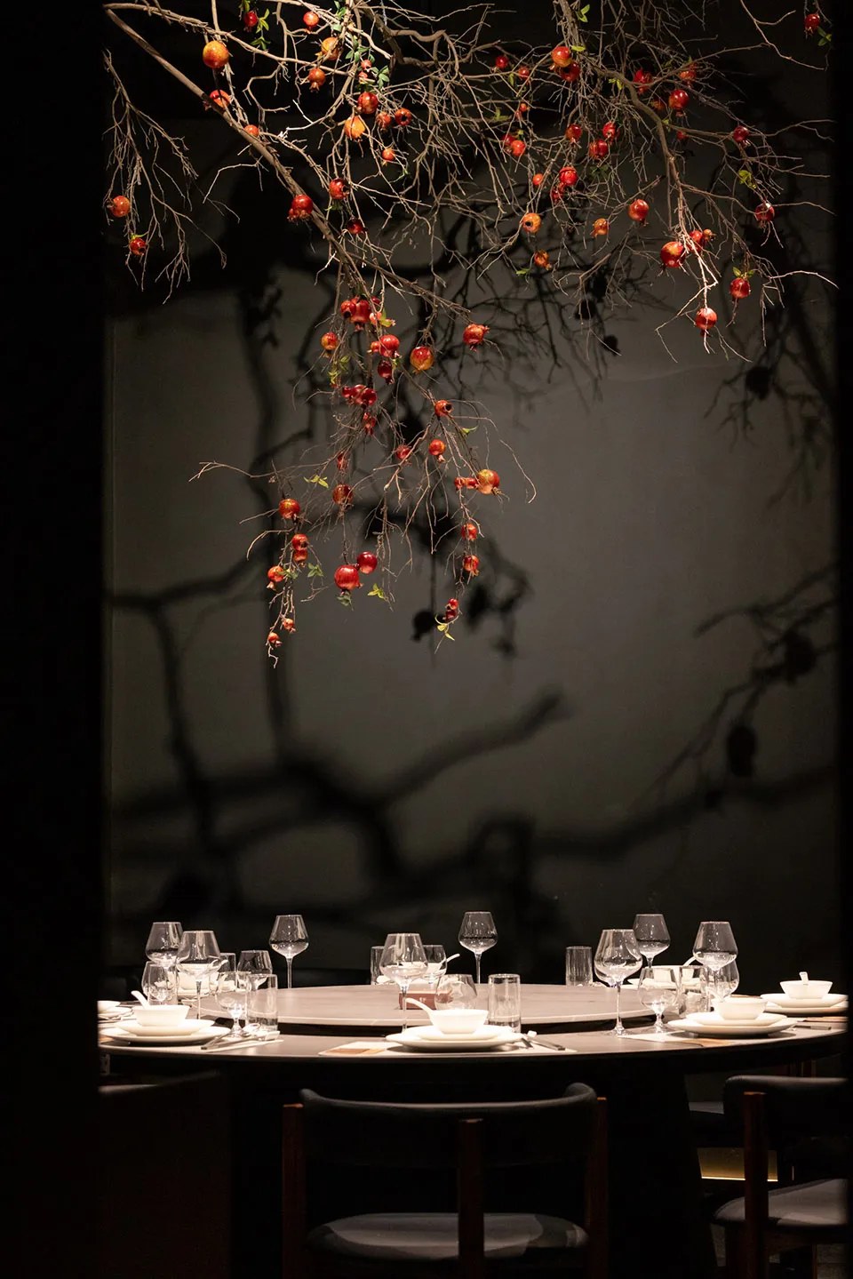 A modern restaurant setting with glass branches adorned with red pomegranates.