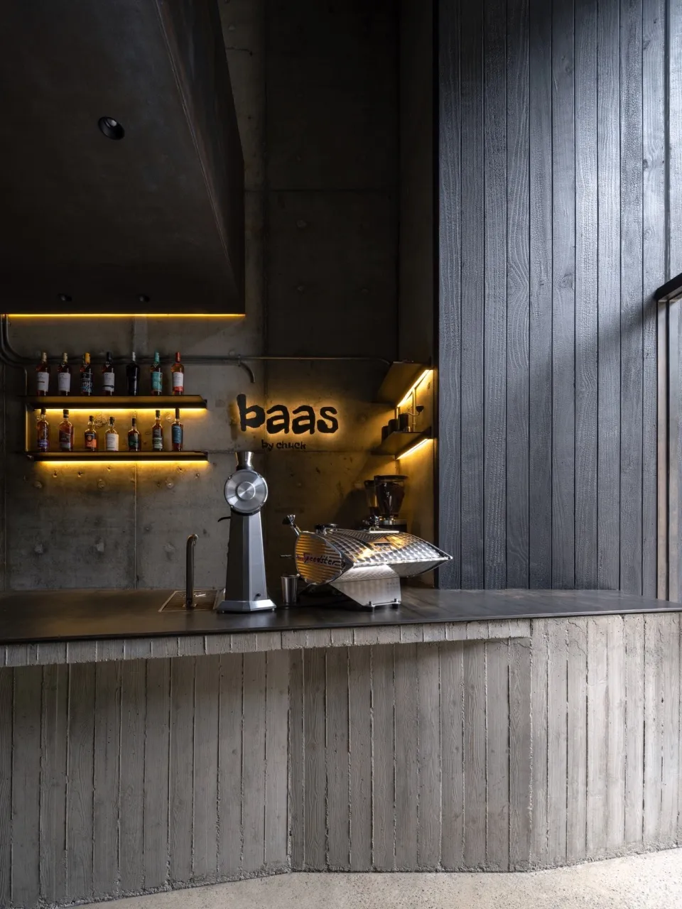 An industrial-style coffee shop bar featuring a concrete bar counter and illuminated shelves.
