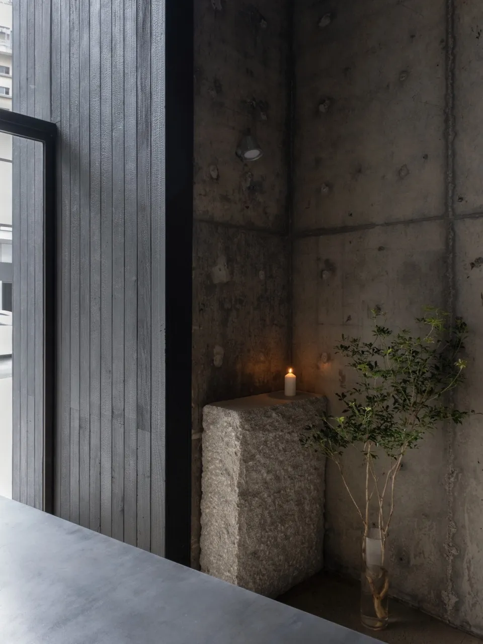 Minimalist interior space featuring a concrete wall and floor, with a candle and plant, creating a serene atmosphere.