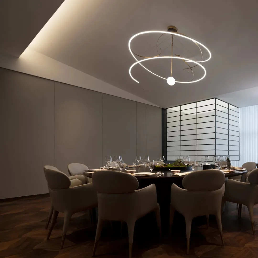 A modern restaurant dining room with a metallic chandelier and dark wooden flooring.