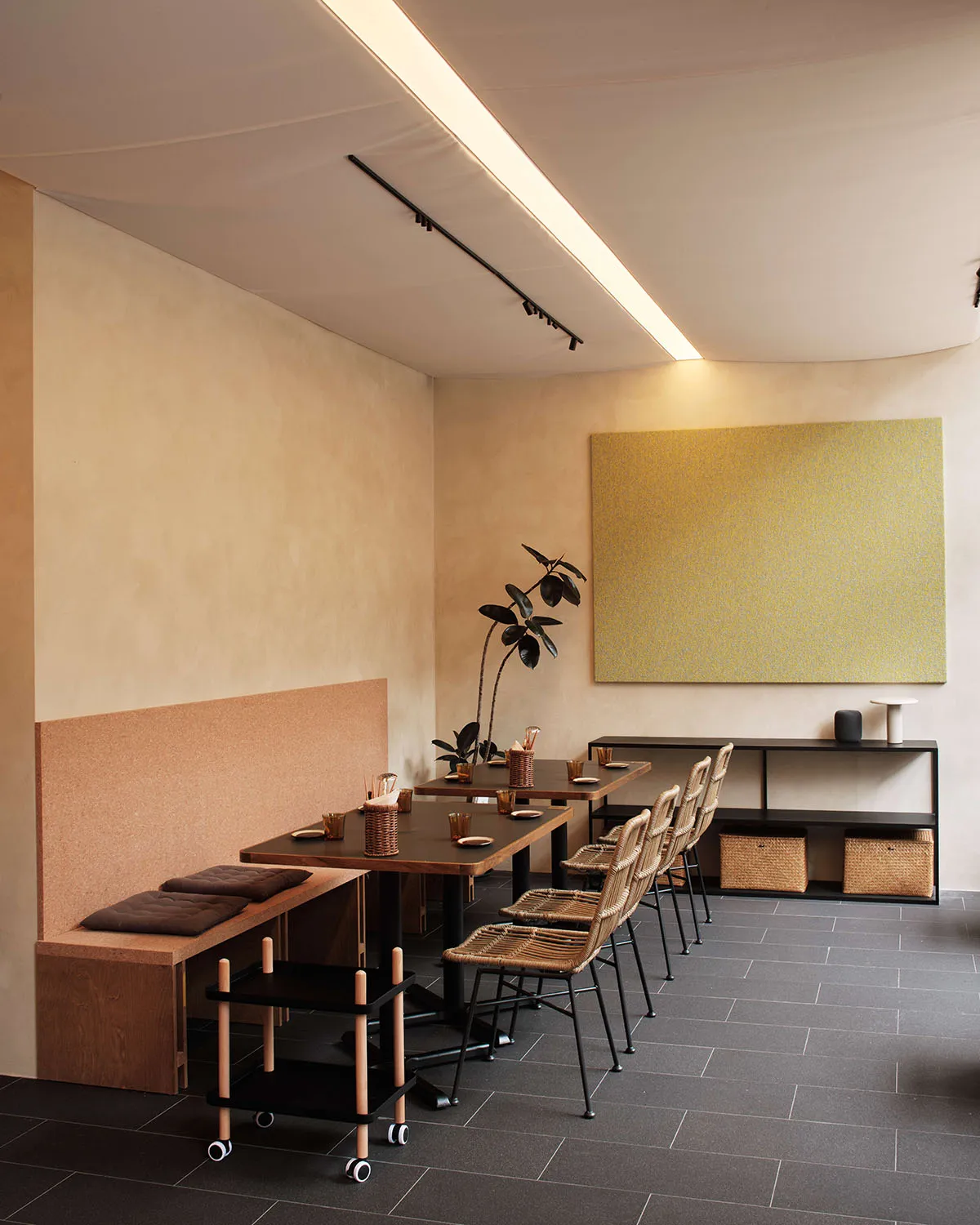 A minimalist restaurant interior featuring wooden tables with woven chairs and concrete accents.