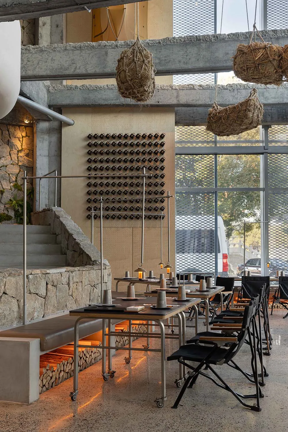 Industrial-style restaurant with minimalist design, concrete walls, and hanging plant baskets.
