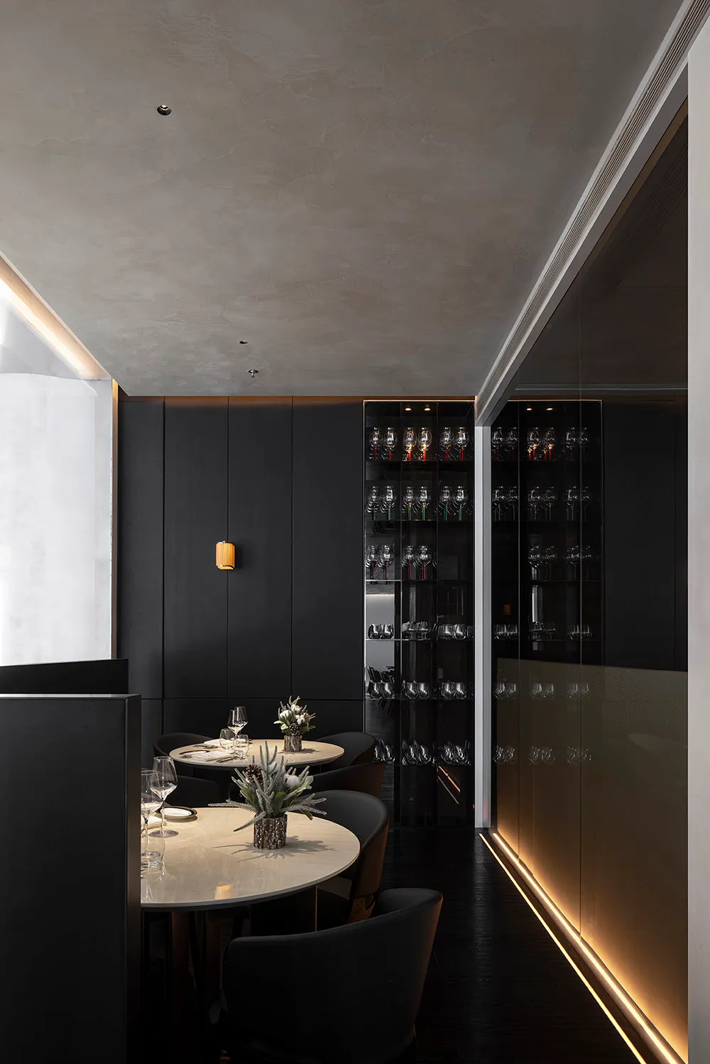 Modern dining room with black metallic wall featuring round tables and chairs, illuminated by subtle ambient lighting.