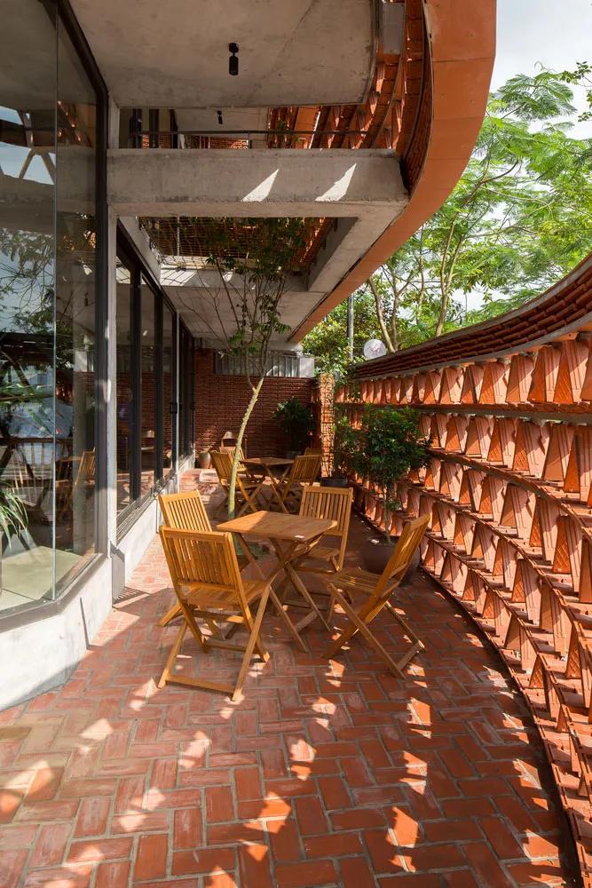A modern, outdoor seating area with wooden chairs and tables, surrounded by brick walls and concrete structural elements.