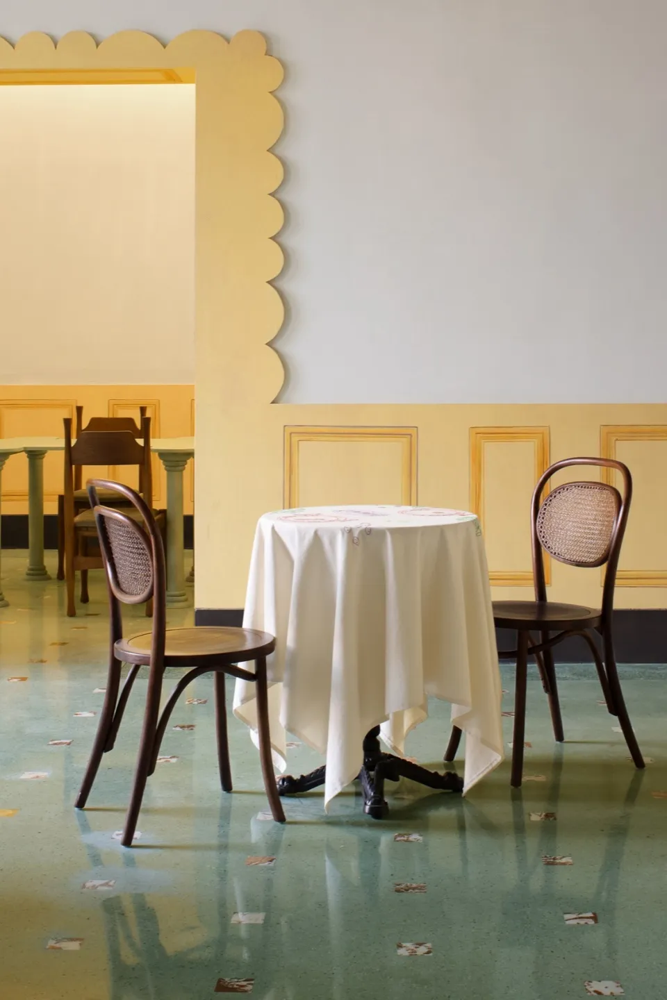 A round table draped with a white cloth, surrounded by wooden chairs, in a restaurant interior.