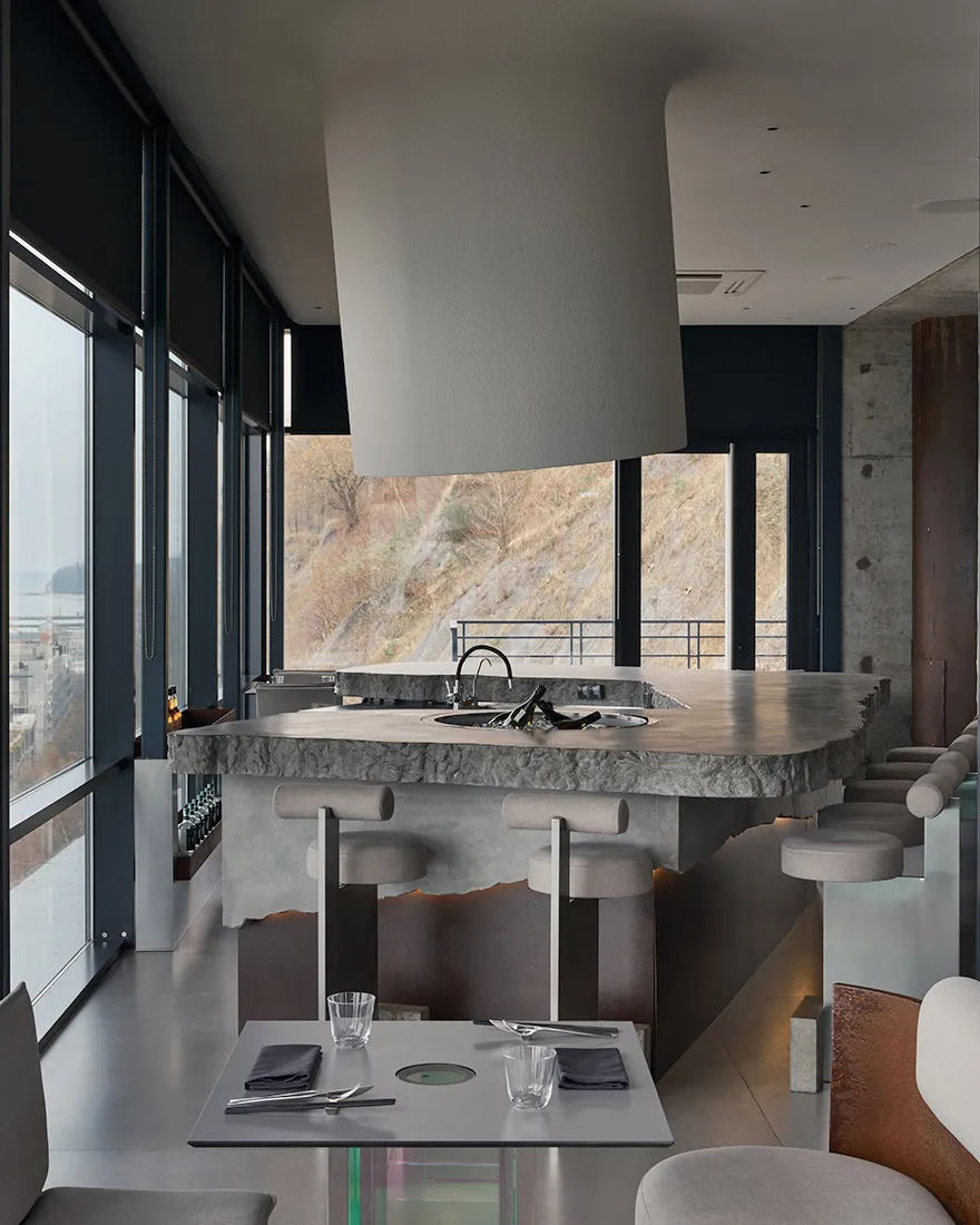 A modern industrial restaurant with a concrete counter, stools, and table setting.