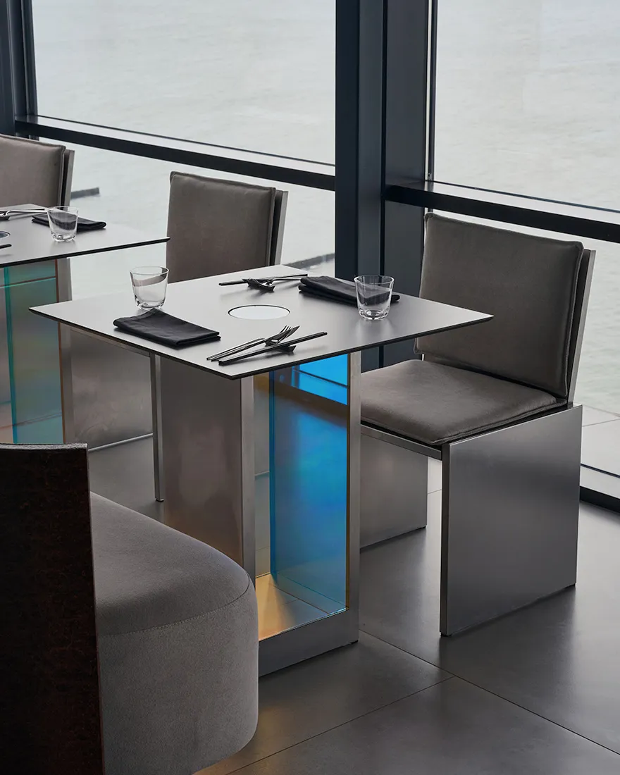 A modern restaurant with sleek metal and glass furniture and a waterfront view.