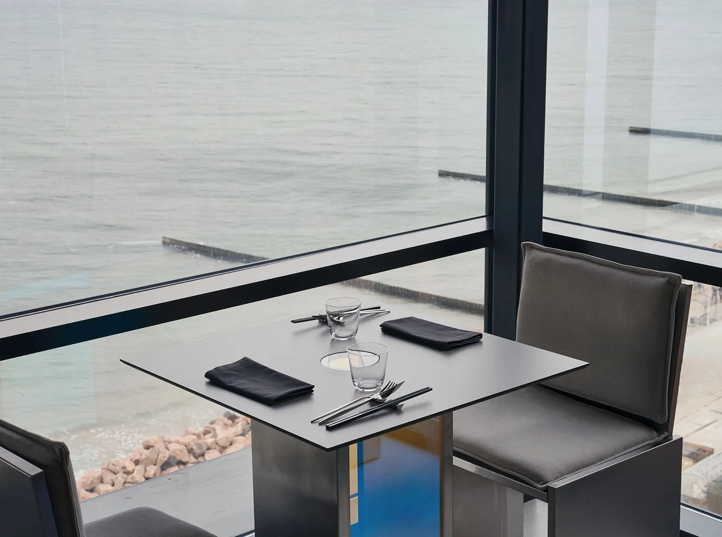 Modern restaurant setting with a metal table, leather chairs, and a stunning sea view.