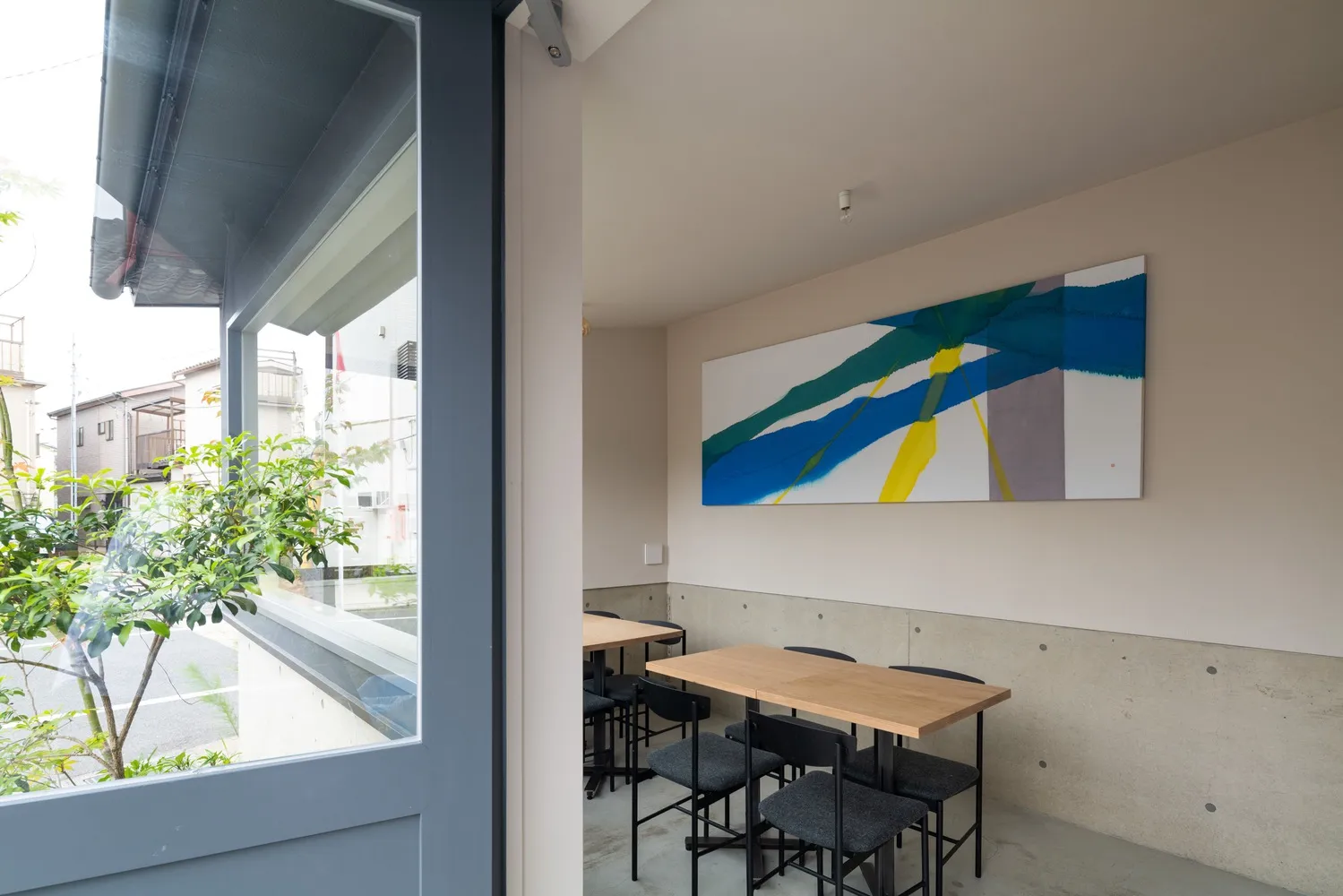 Modern cafe interior with concrete walls, wooden tables, and black chairs.