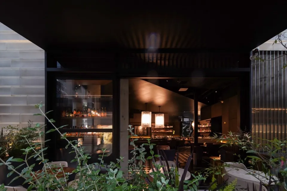Modern restaurant interior with concrete walls, glass windows, and a bar area.