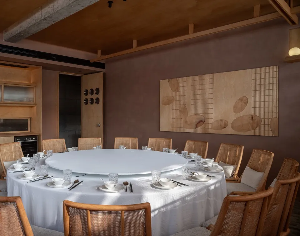 Circular table with white tablecloth surrounded by wooden chairs in a modern restaurant interior with concrete walls and larg