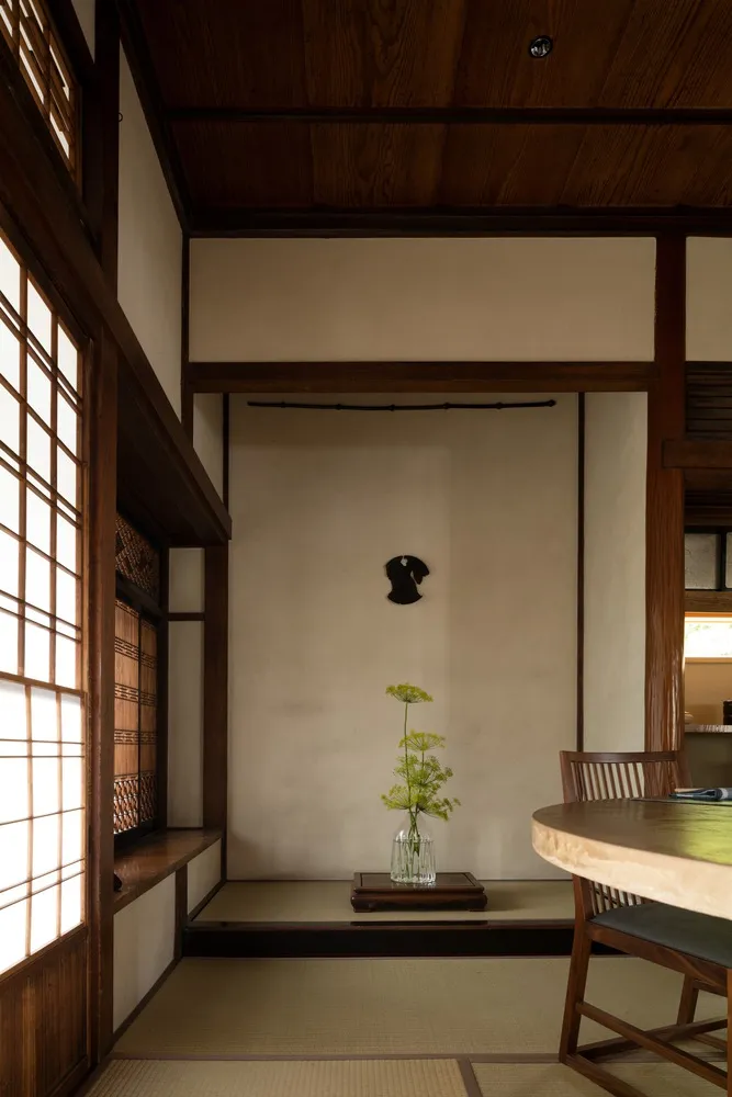 A modern living room interior with wooden walls and floor, featuring a vase with green flowers on a low table and a window wi