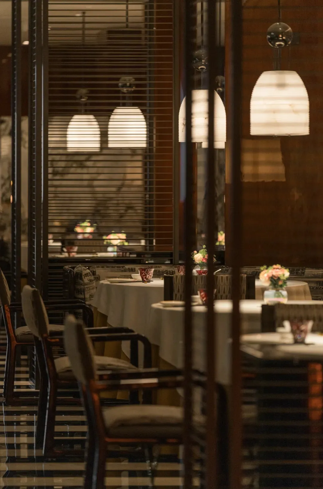 Modern restaurant interior with dark lighting and natural light, featuring tables, chairs, and pendant lights.