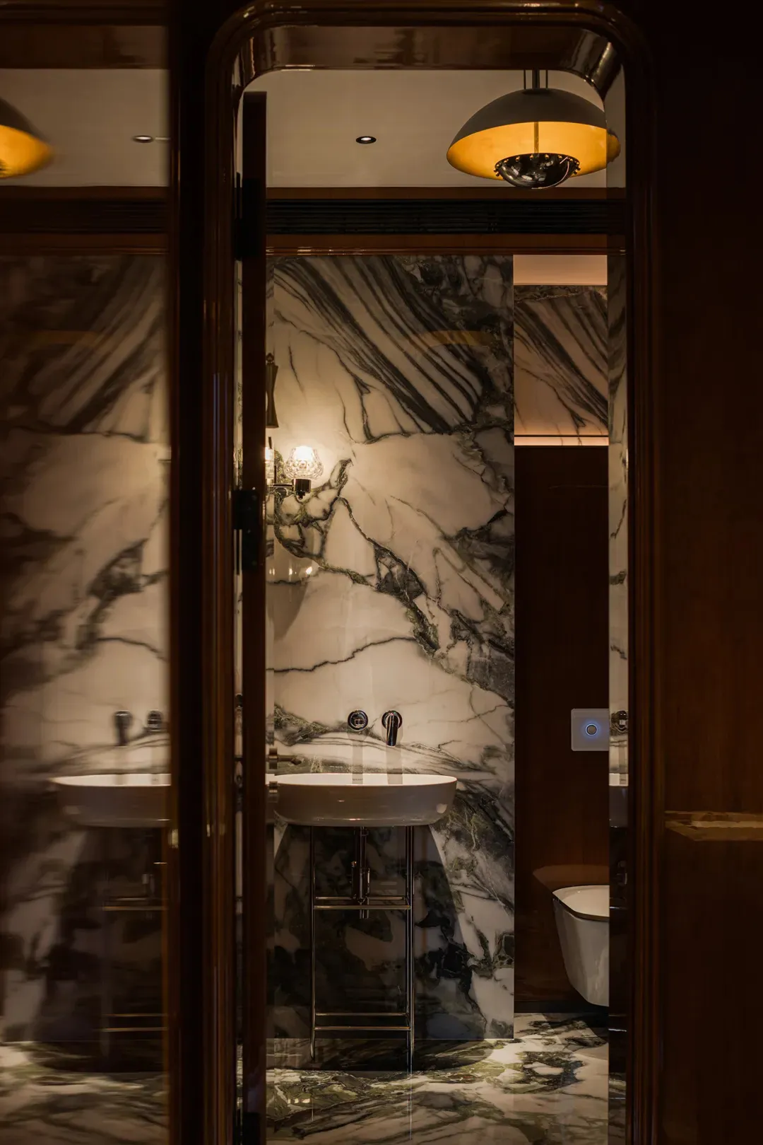 Modern bathroom with marble walls and floor, featuring a white sink and toilet.