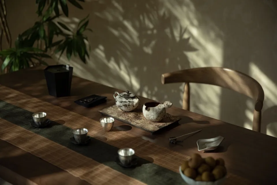 A wooden table with ceramic tea pots and cups, surrounded by greenery and natural light.