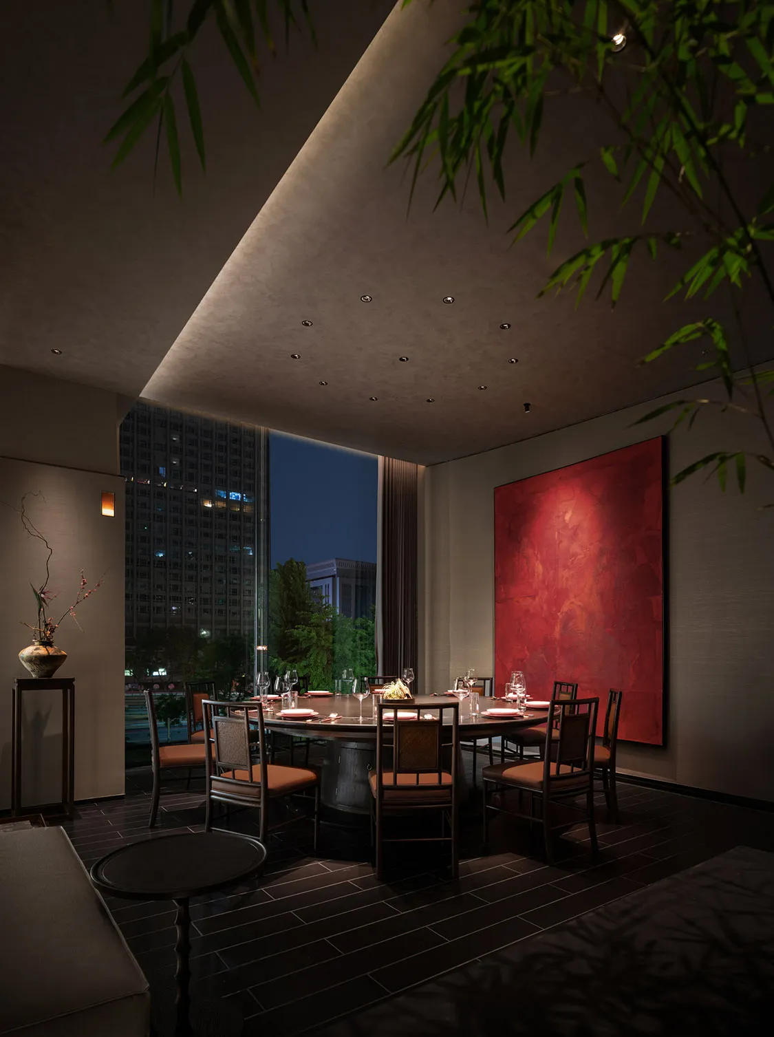 A modern dining room featuring a floating ceiling, round wooden table, and glass windows with city view.