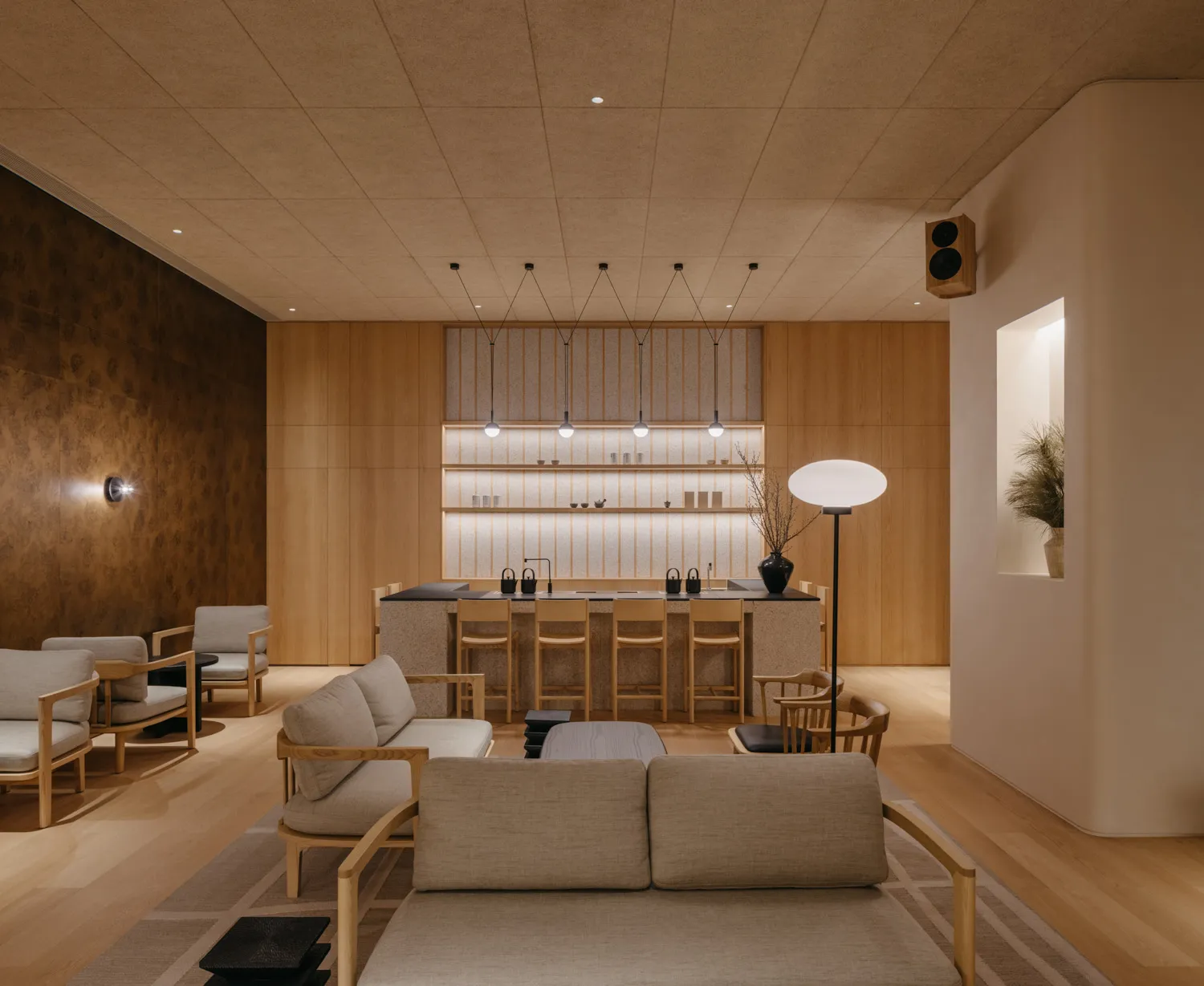 A modern living room featuring a bar area with light wood cabinets, terrazzo countertops, and concrete flooring.