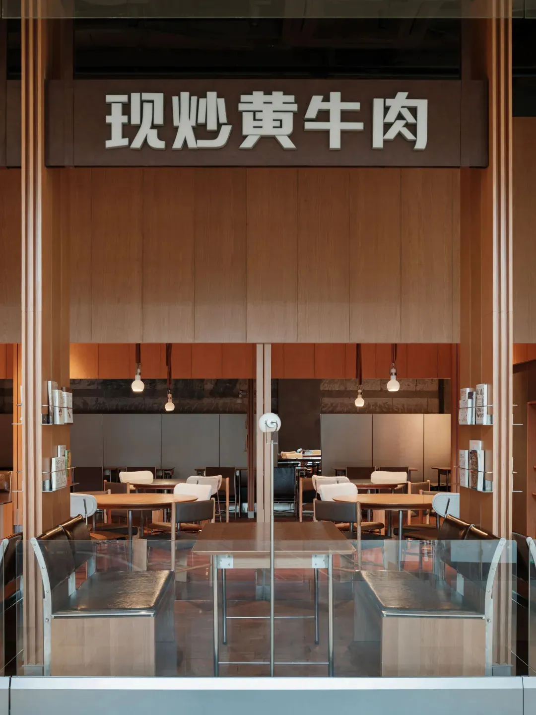 Modern restaurant interior with wooden tables, white chairs, and glass partitions.