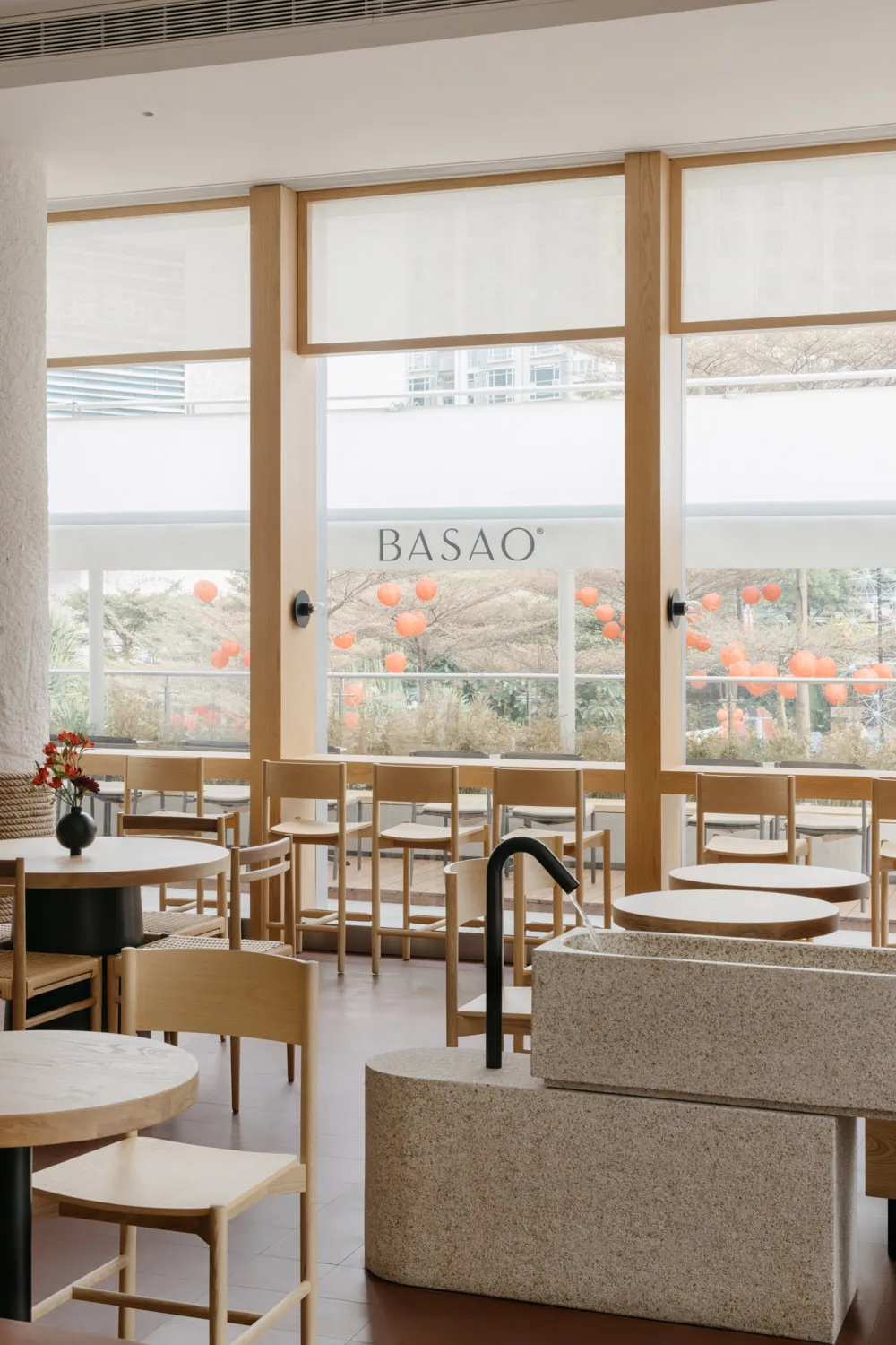 Contemporary restaurant interior featuring wooden tables and chairs, stone sink, and minimalist design.
