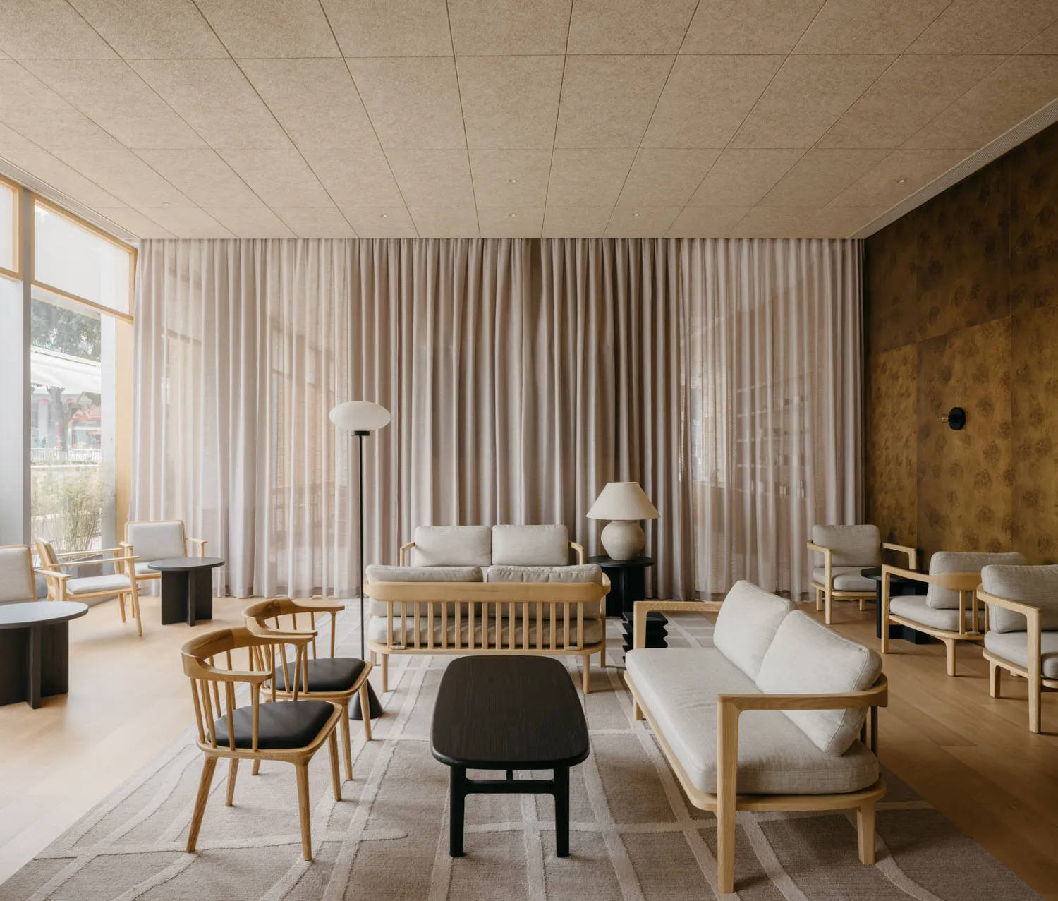 A minimalist living room with fabric couches, wooden chairs, and glass coffee table.