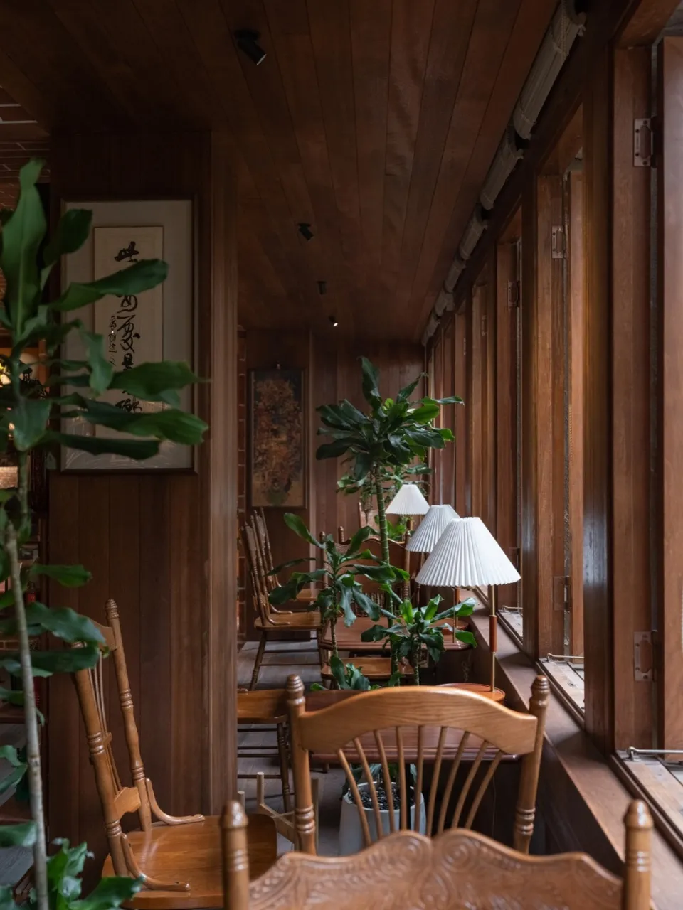 A cozy cafe interior featuring wooden chairs, glass windows, and fabric lampshades.
