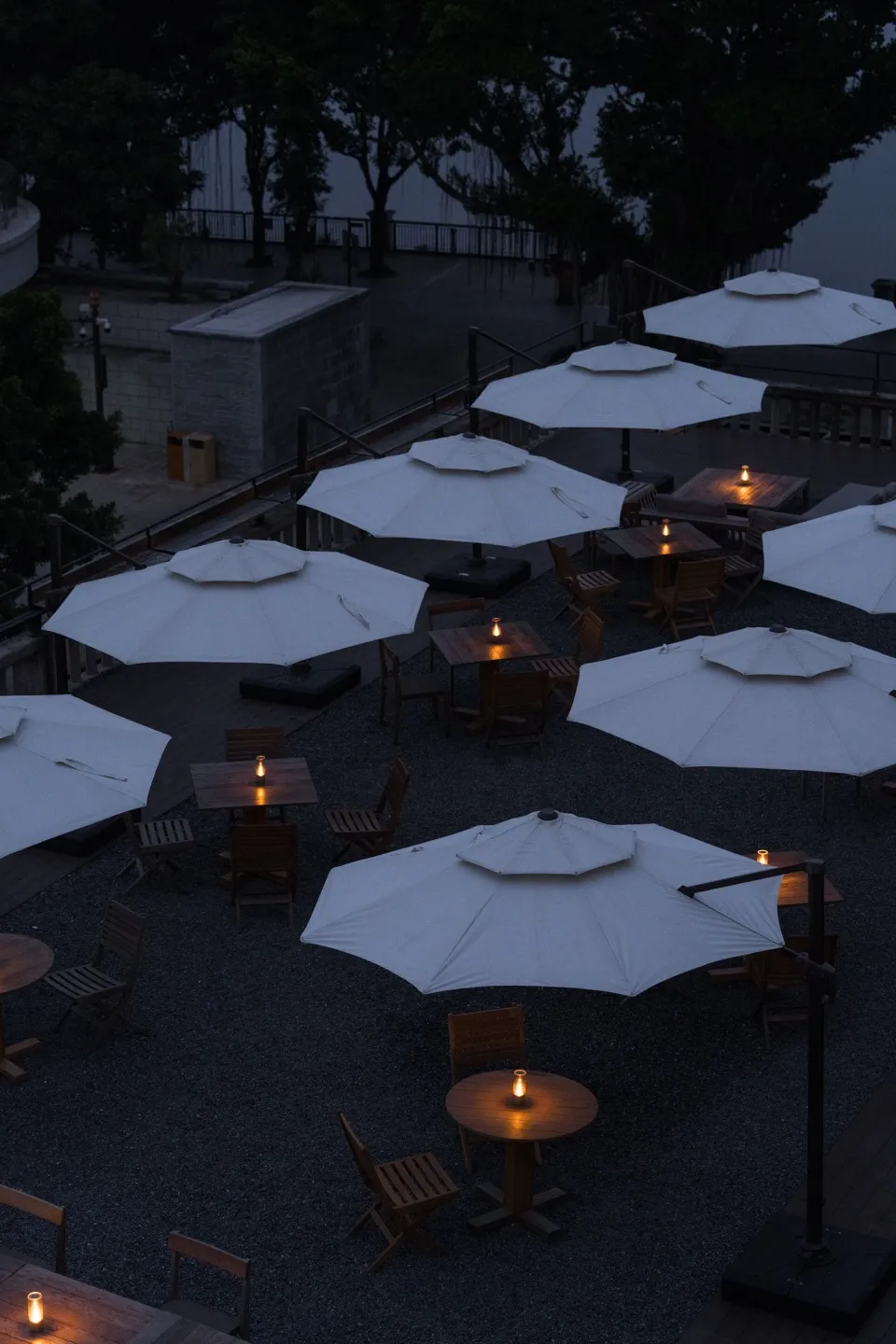 Outdoor seating arrangement of wooden tables and chairs under white umbrellas with candle lights.