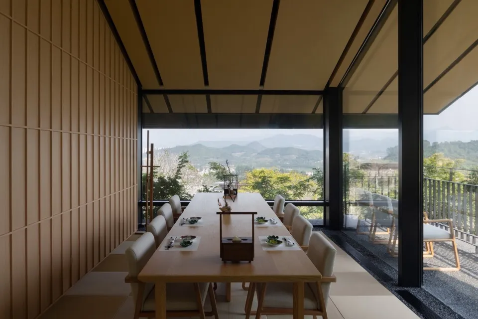 Minimalist dining room with wooden furniture and a view of mountains through large windows.